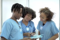 Three African American medical professionals stand looking at a chart in a hospital setting.