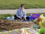 Woman with short hair and sunglasses, sitting on the ground cutting long brown reeds.